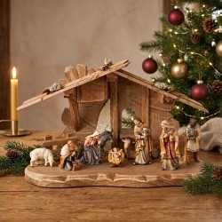 Presepe Kostner con capanna decorato accanto all'albero di Natale e candela